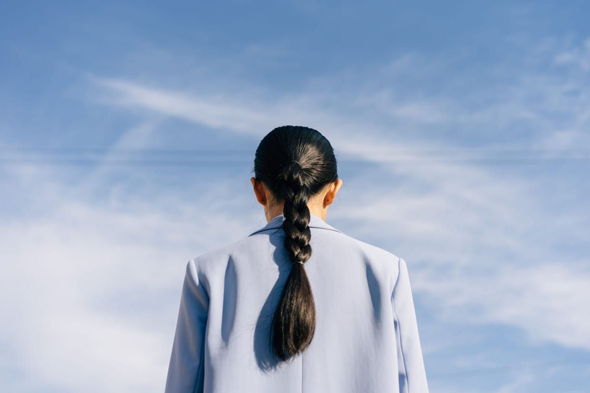A woman seen from behind with her dark hair in one long, loose braid against a blue sky