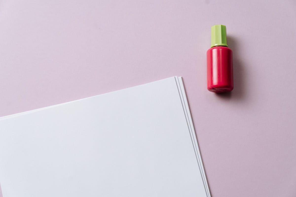 A bottle of pink nail polish next to a stack of blank paper on a pink table